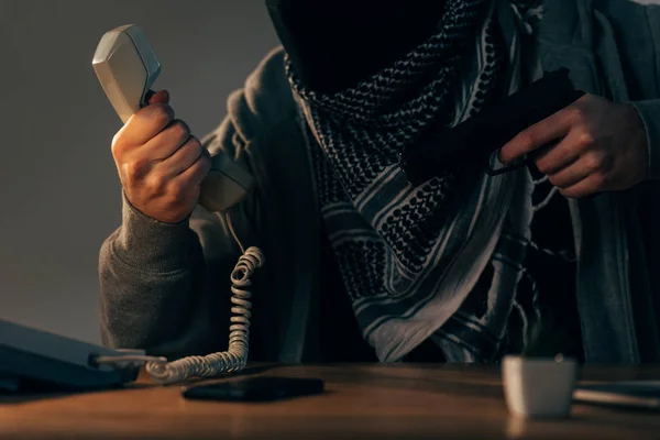 Обрезанный вид на телефон террориста и пистолет за столом — стоковое фото