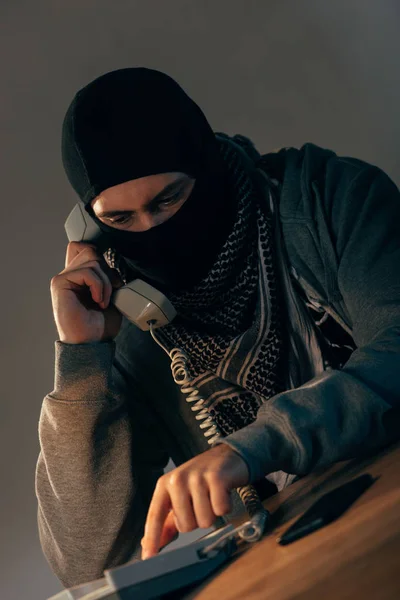 Терорист у чорній масці розмовляє по телефону в кімнаті — стокове фото