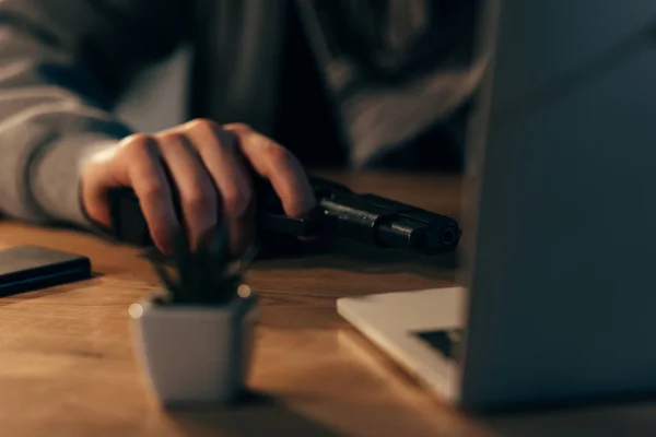 Vista parcial del terrorista con arma de fuego usando portátil en la mesa - foto de stock