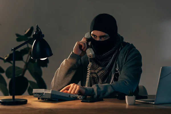 Серьезный преступник в черной маске разговаривает по телефону в номере — стоковое фото