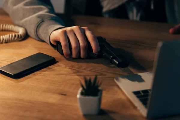 Vista parcial do criminoso com arma e smartphone na mesa de madeira — Fotografia de Stock