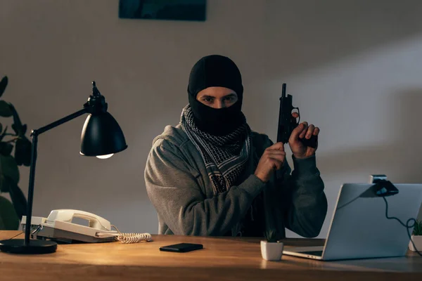 Злочинець у чорній масці дивиться на камеру і заряджає пістолет в кімнаті — стокове фото