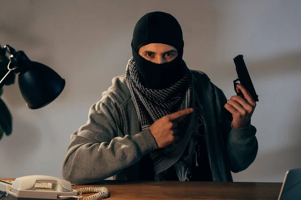 Terrorist in black mask pointing with finger at gun — Stock Photo