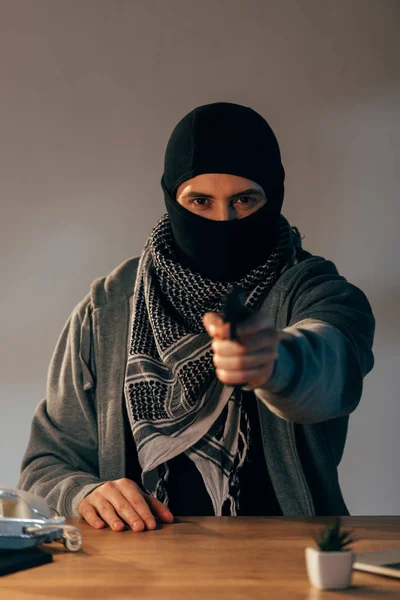 Concentrated criminal in black mask aiming gun at camera — Stock Photo