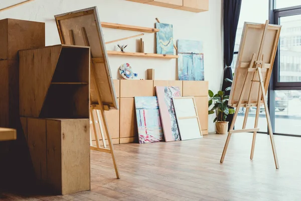 Spazioso studio di pittura leggera con pavimento in legno, armadi, scaffali, cavalletti e dipinti — Foto stock