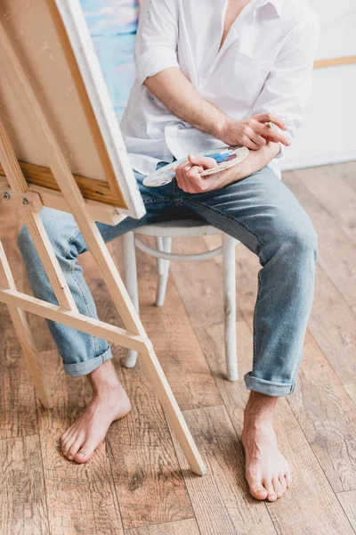 Vue partielle de l'artiste pieds nus assis au chevalet avec toile — Photo de stock