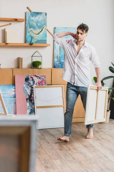 Selective focus of handsome artist in white shirt and blue jeans carrying canvas — Stock Photo