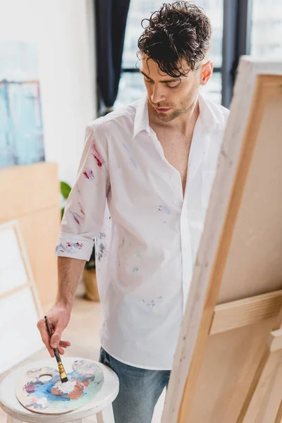 Foco seletivo do artista em camisa branca manchada com tintas de mistura de tinta na paleta — Fotografia de Stock