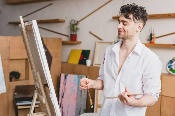 Focus sélectif de l'artiste souriant en chemise blanche et jean bleu regardant la toile — Photo de stock