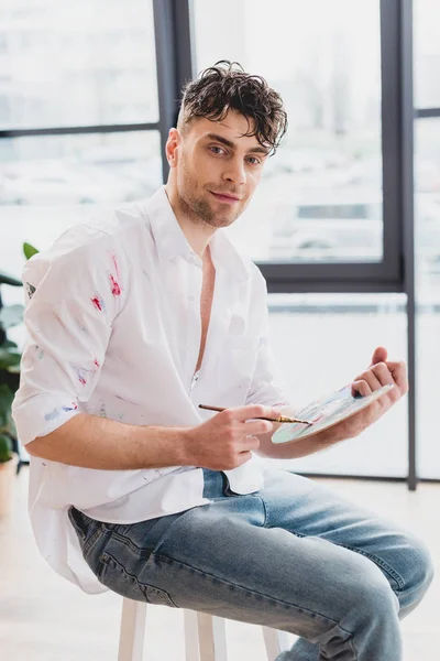 Artiste souriant avec palette et pinceau regardant la caméra — Photo de stock