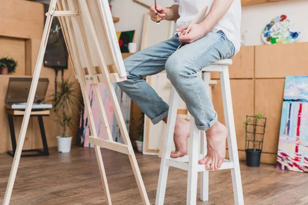 Vista parcial del artista descalzo sentado en la silla alta en el estudio de pintura - foto de stock