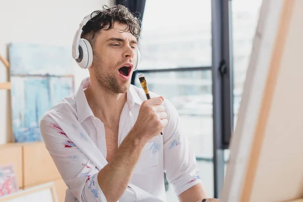 Foco seletivo de artista bonito em fones de ouvido, cantando com pincel — Fotografia de Stock