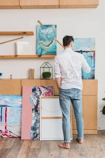 Back view pf barefoot artist in white shirt and blue jeans standing in painting studio — Stock Photo
