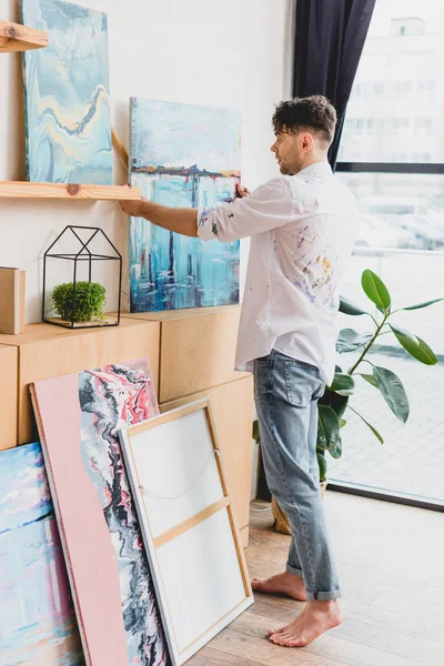 Artista guapo en camisa blanca y pantalones vaqueros azules de pie en la galería de luz - foto de stock
