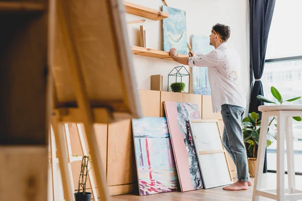 Selective focus of artist in white shirt and blue jeans standing in light gallery — Stock Photo