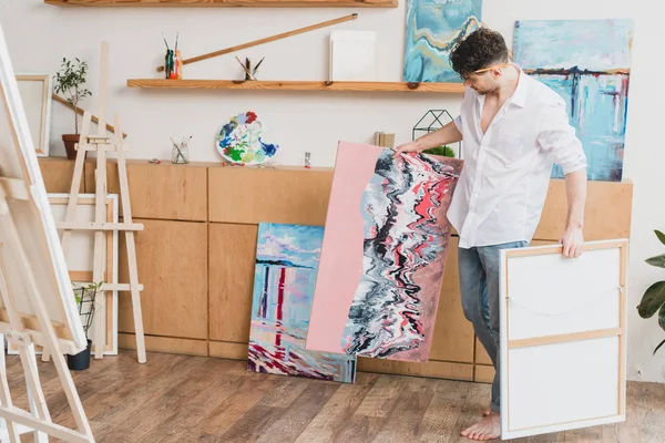 Artista descalzo en camisa blanca y vaqueros azules llevando pinturas en la galería - foto de stock