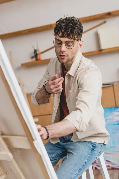 Selektiver Fokus des gutaussehenden Künstlers in Brillenmalerei auf Leinwand — Stockfoto