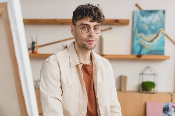 Selective focus of handsome artist in eyeglasses looking at camera — Stock Photo