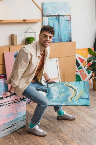 Artista guapo en camisa rosa y pantalones vaqueros azules sosteniendo imagen colorida - foto de stock