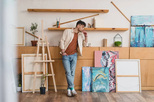 Selective focus of handsome artist in pink shirt and blue jeans standing in spacious gallery — Stock Photo