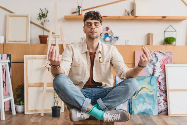 Verträumter Künstler mit geschlossenen Augen sitzt in Lotus-Pose in Galerie — Stockfoto