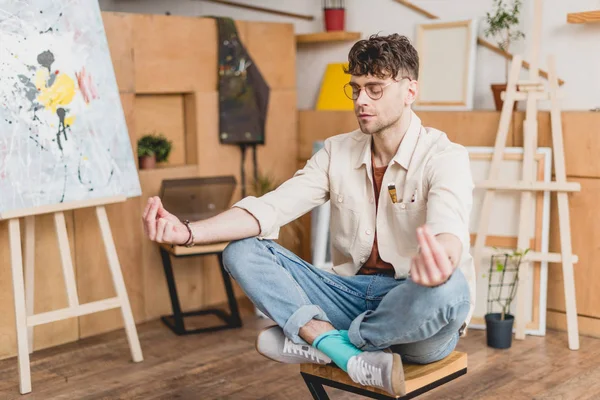 Enfoque selectivo de artista de ensueño con los ojos cerrados sentado en la pose de loto en la galería - foto de stock