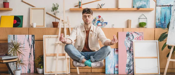 Panoramic shot of artist with closed eyes levitating in lotus pose in gallery — Stock Photo