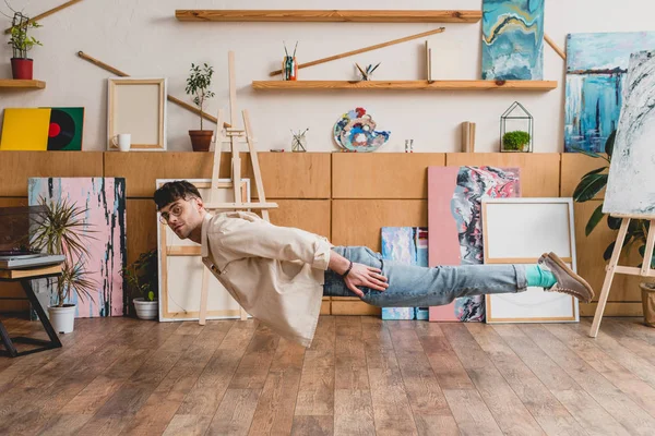 Dreamy artist with closed eyes levitating over wooden floor in painting studio — Stock Photo