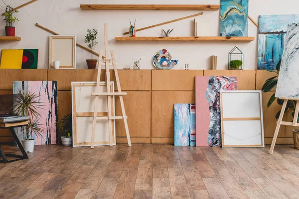 Просторная студия легкой живописи с деревянными шкафами, полками, мольбертами и картинами — стоковое фото