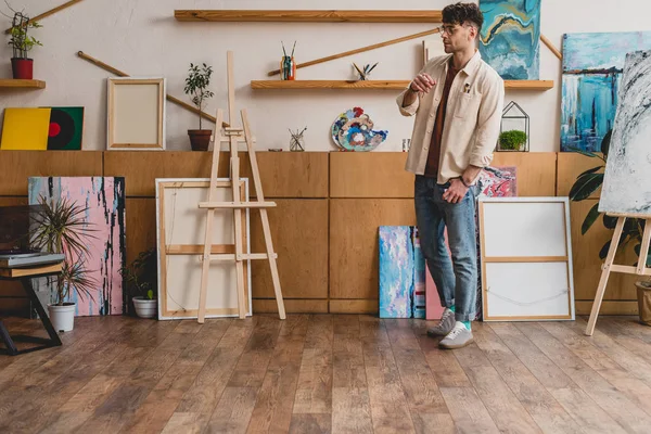 Artista guapo en camisa rosa y vaqueros azules de pie en amplia galería de luz — Stock Photo