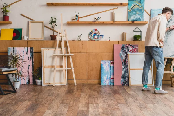 Artist in pink shirt and blue jeans standing in spacious painting studio — Stock Photo