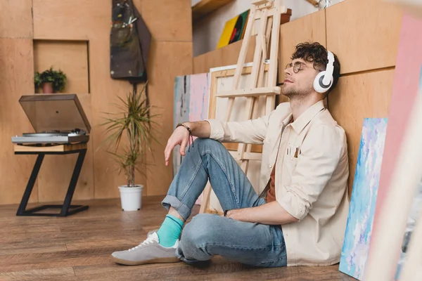 Schöner Künstler mit Kopfhörern auf dem Boden sitzend und mit geschlossenen Augen Musik hörend — Stockfoto