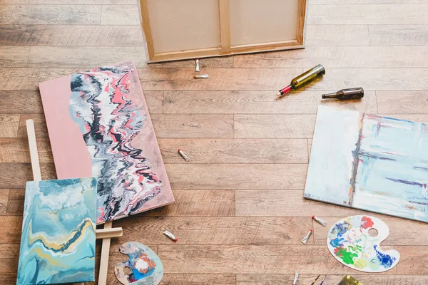 High angle view of paintings, draw utensils and empty bottles on wooden floor in painting studio — Stock Photo