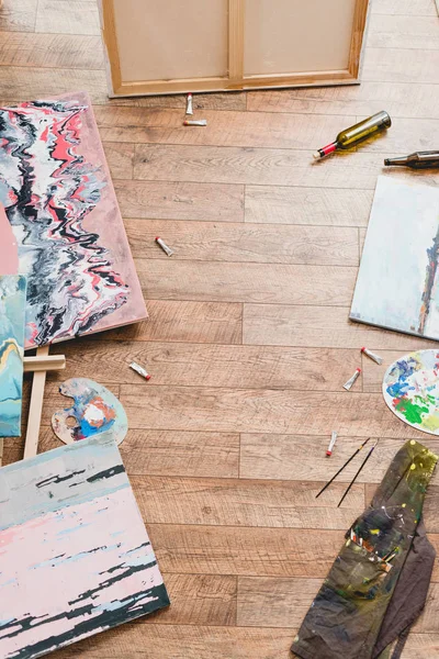 High angle view of paintings, draw utensils and empty bottles on wooden floor in gallery — Stock Photo