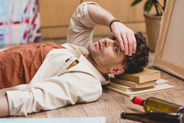 Selective focus of exhausted artist laying with hand on head and looking at camera — Stock Photo