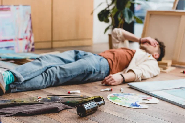 Selective focus of tired artist lying on floor with hand on face — Stock Photo