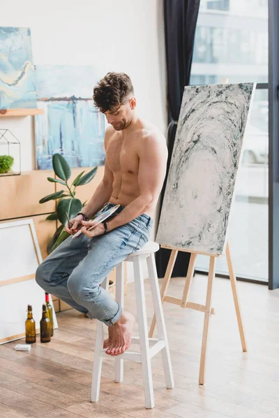 Artiste beau à moitié nu assis sur la chaise dans le studio de peinture — Photo de stock