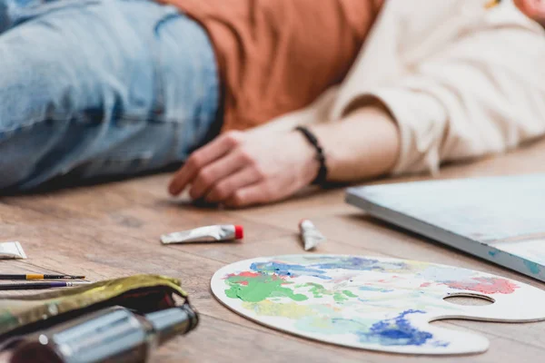 Selective focus of artist lying on floor surrounded with draw utensils — Stock Photo