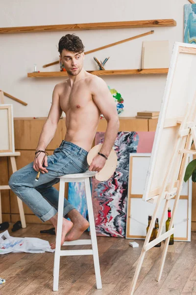 Handsome half-naked artist sitting in high chair in gallery — Stock Photo