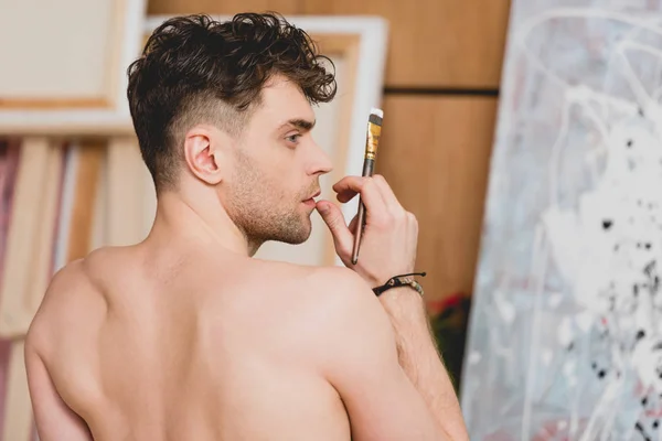 Selective focus of handsome half-naked artist holding paintbrush — Stock Photo