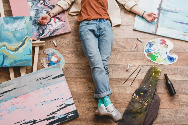 Partial view of artist lying of floor, surrounded with painting and draw utensils — Stock Photo