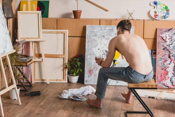 Artiste à moitié nu en jeans bleu assis sur une chaise dans la galerie — Photo de stock