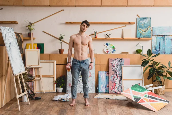 Bel mezzo nudo artista in jeans blu in piedi in galleria spaziosa — Foto stock