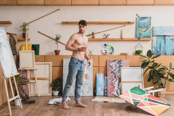 Artista semidesnudo guapo en vaqueros azules de pie en la galería espaciosa - foto de stock