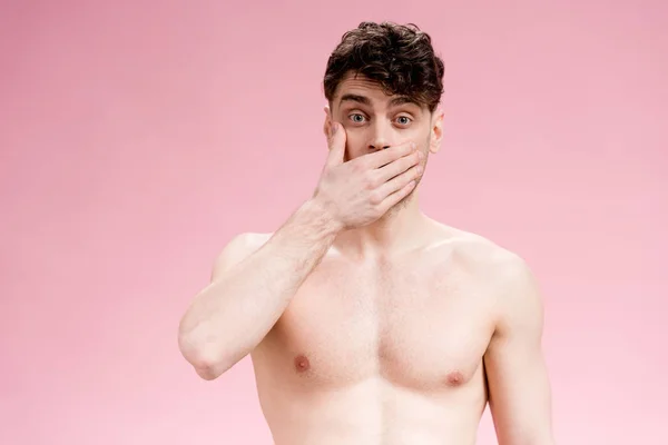 Handsome, surprised brunette man covering mouth with hand on pink — Stock Photo