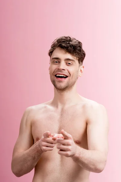 Веселый брюнетка мужчина указывая пальцами и глядя на камеру на розовый — стоковое фото
