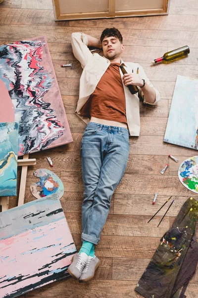 Над головой вид художника, лежащего на полу и держащего в руках бутылку алкоголя — стоковое фото