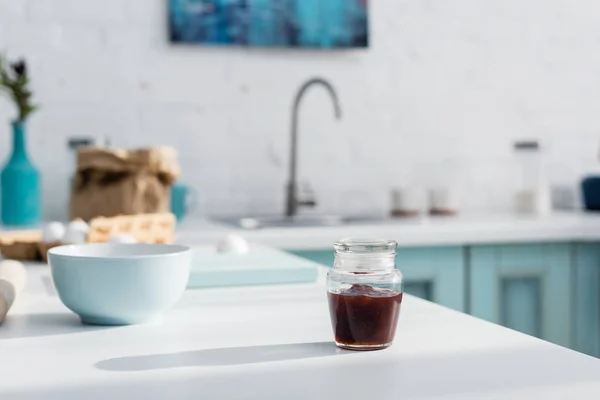 Glas mit schmackhafter roter Marmelade neben Schüssel auf Küchentisch — Stockfoto