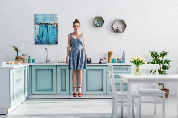 Sorrindo menina bonita levitando no ar em turquesa e cozinha branca — Fotografia de Stock