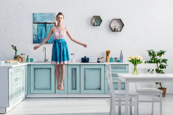Красивая босиком девушка в фартуке левитирует в воздухе на кухне — стоковое фото